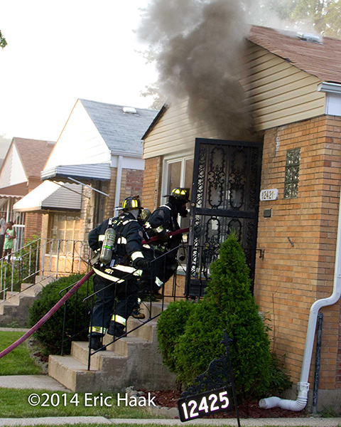 firemen enter a house with thick smoke coming out