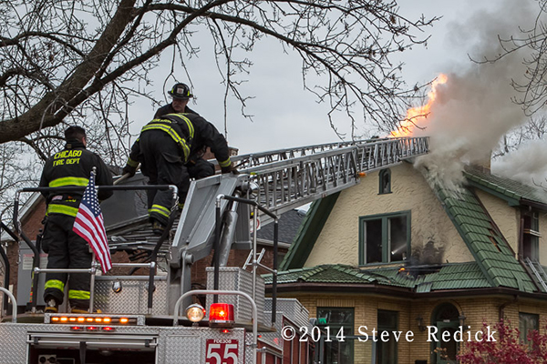 firemen on a ladder with fire through the roof of a house