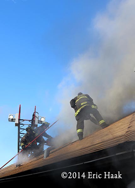 firemen with saw on roof at house fire