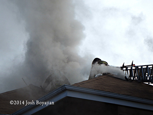 firemen with saw on roof at house fire
