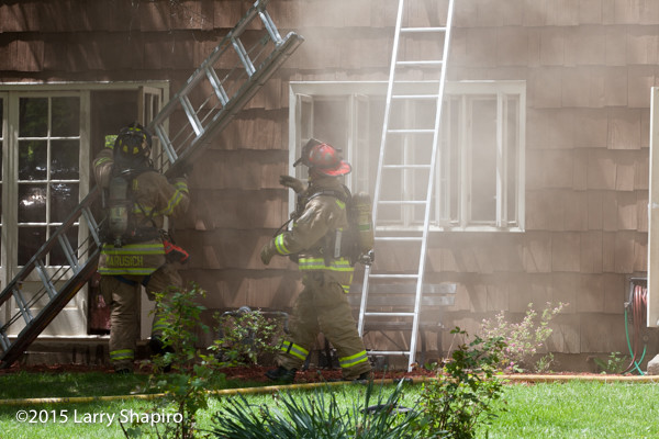 firemen raise a ladder in smoke at house fire