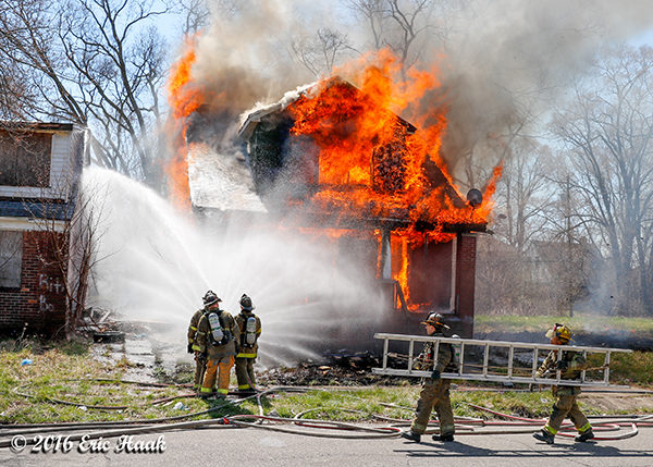 firemen creating a water curtain at a vacant house fully engulfed in flames