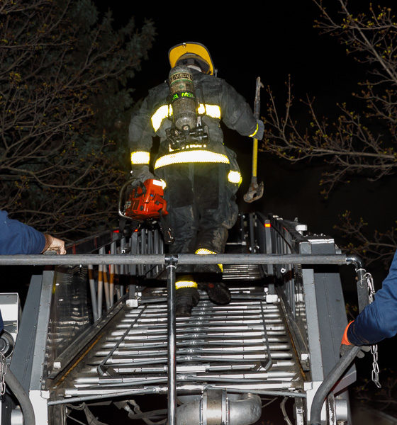 firefighter climbs aerial ladder at night