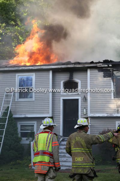 firefighters battle house with flames through the roof