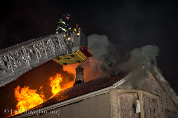 heavy flames and smoke through roof of a house at night