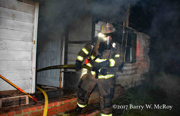 firefighter with full PPE exits house fire with a hose line